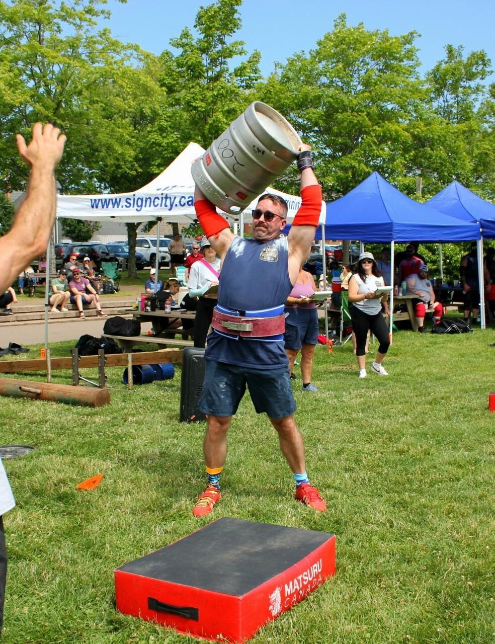 Josh Dunbar lifting a keg overhead at an outdoor strongman competition