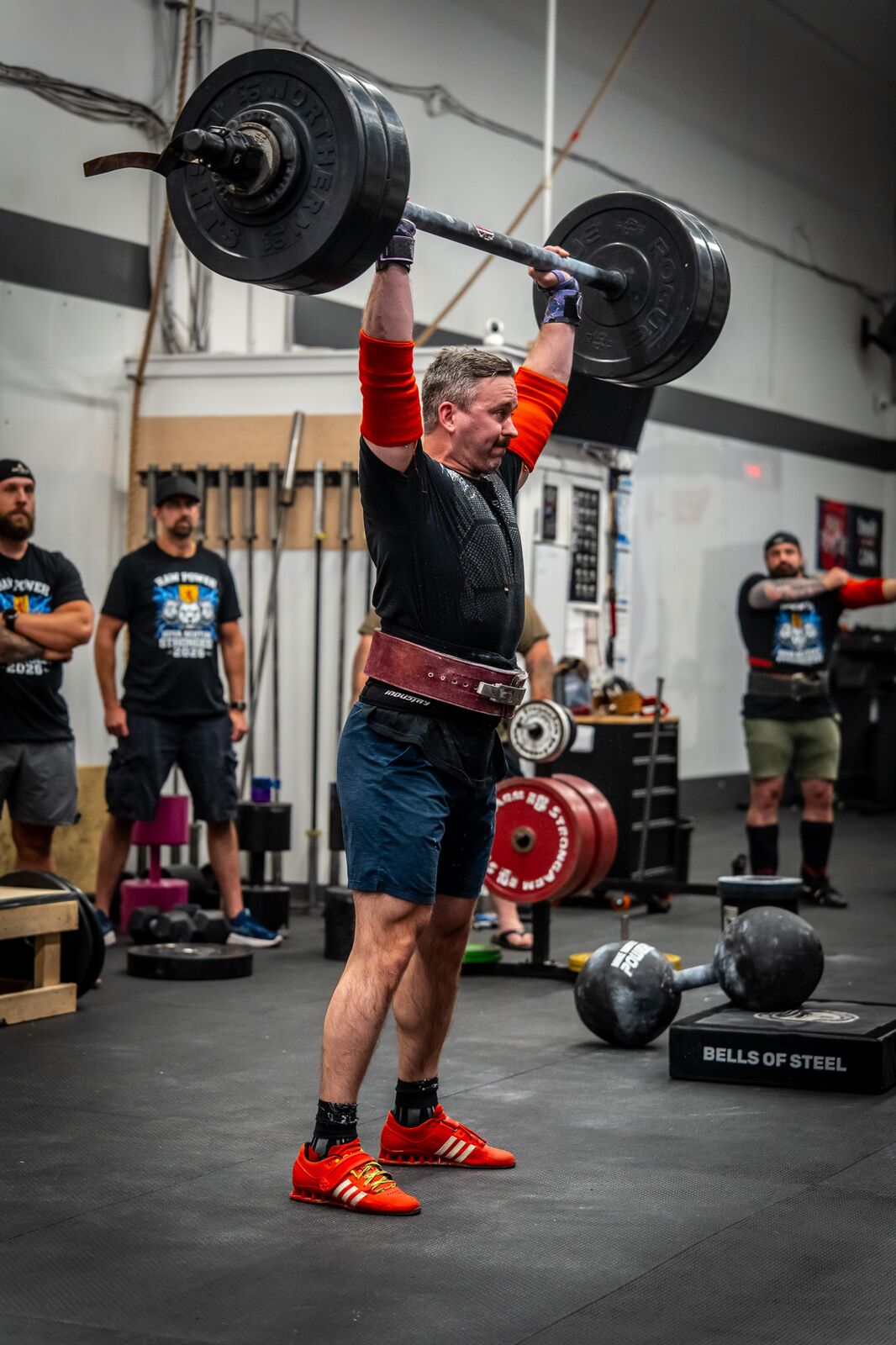 Josh Dunbar pressing a barbell overhead in a strongman gym